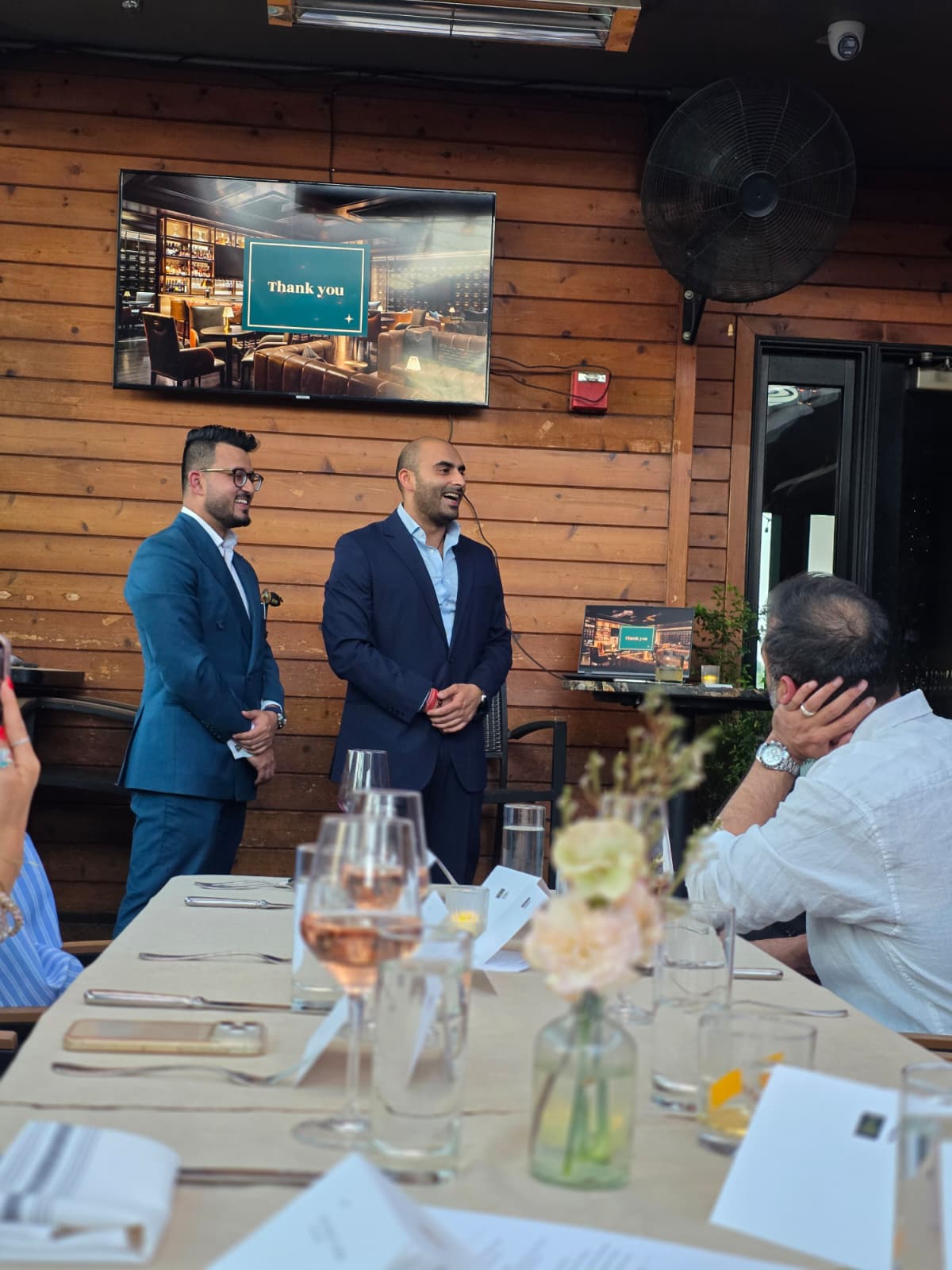Hosts welcoming members at a cigar and whiskey dinner with a thank you slide on screen